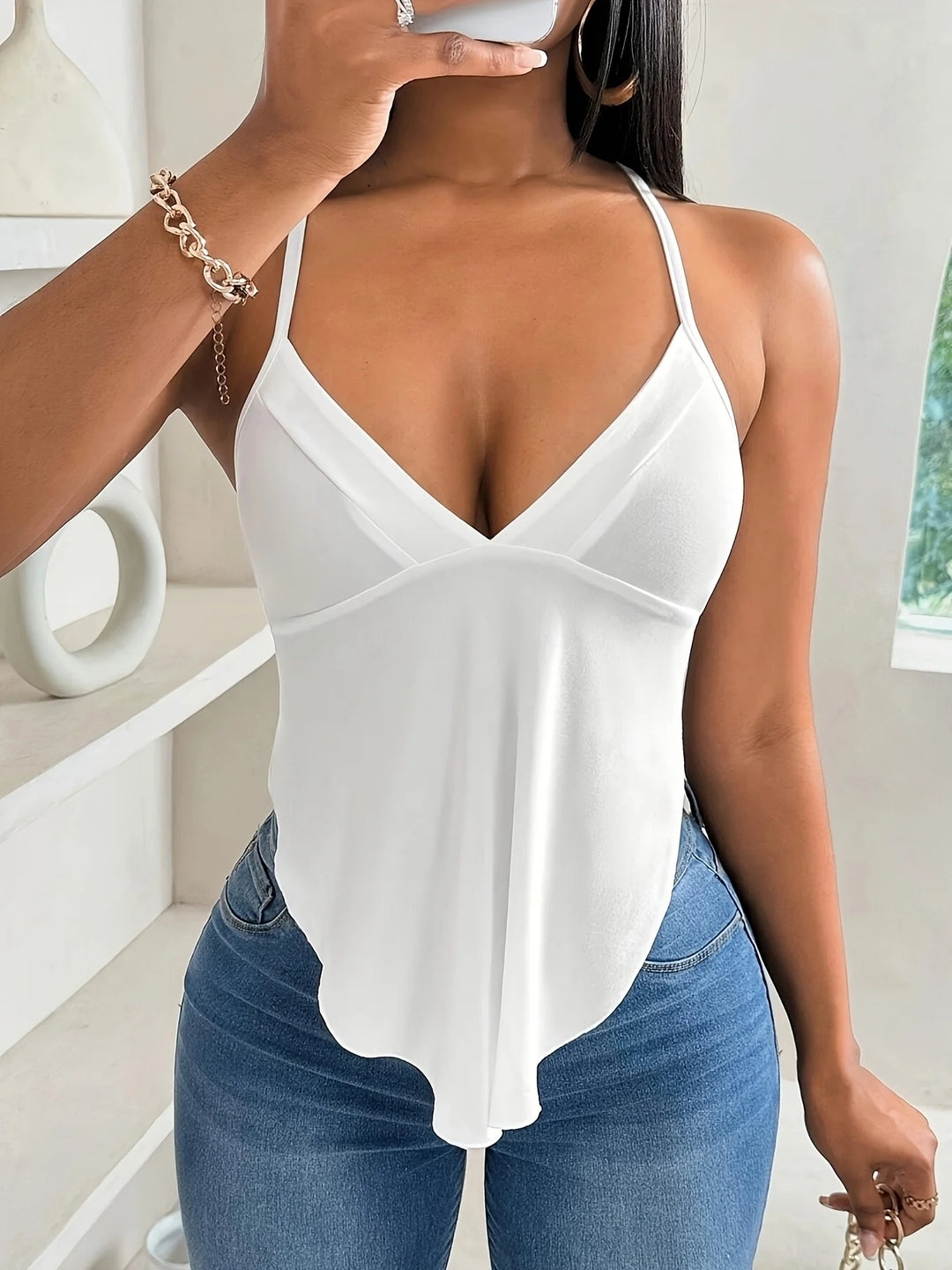 Woman wearing a white strappy top and blue jeans indoors.