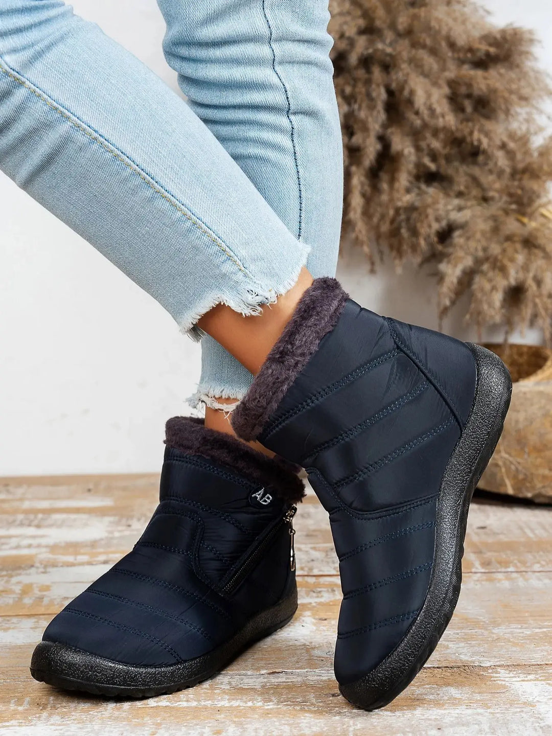 Navy blue winter boots with fur lining worn with light blue jeans on a wooden floor.