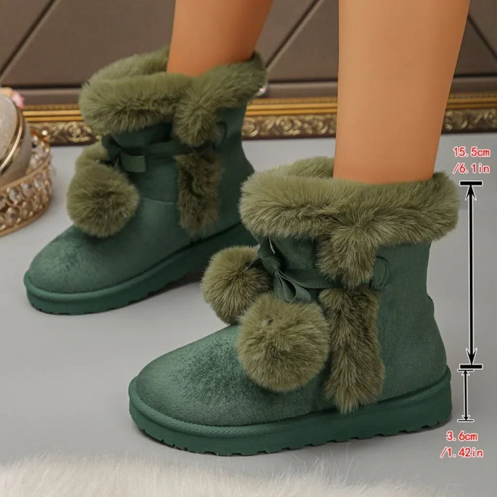 Green faux-fur ankle boots with bow and pom-pom details, shown on a doll's legs against a neutral indoor background.