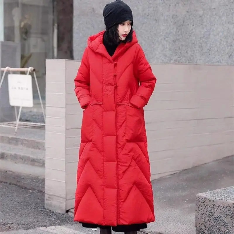 Person wearing a long red coat standing outdoors against a neutral background