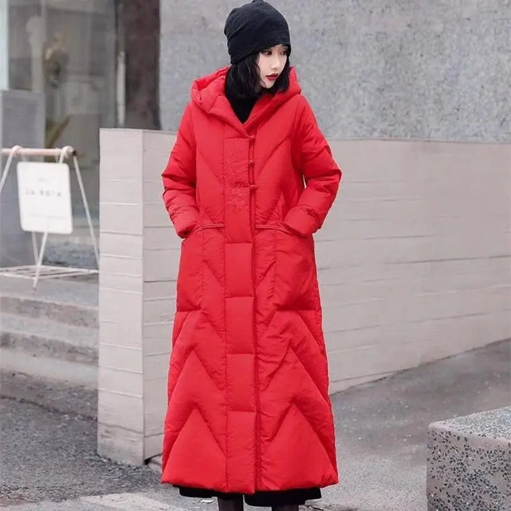 Person wearing a long red coat standing outdoors against a neutral background