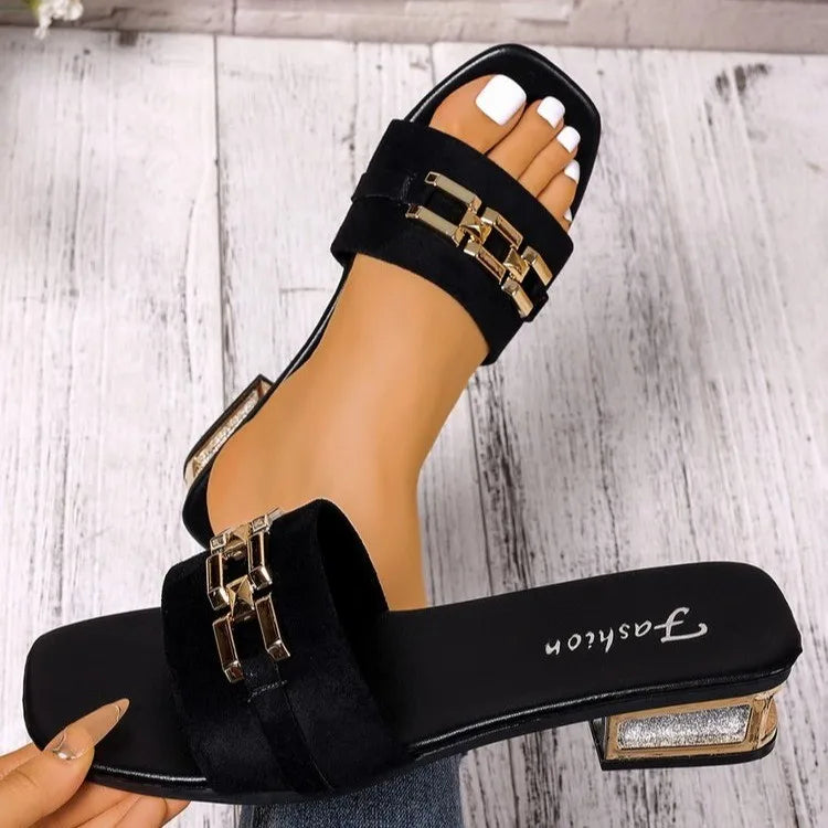 Black sandal with gold accents on a wooden floor