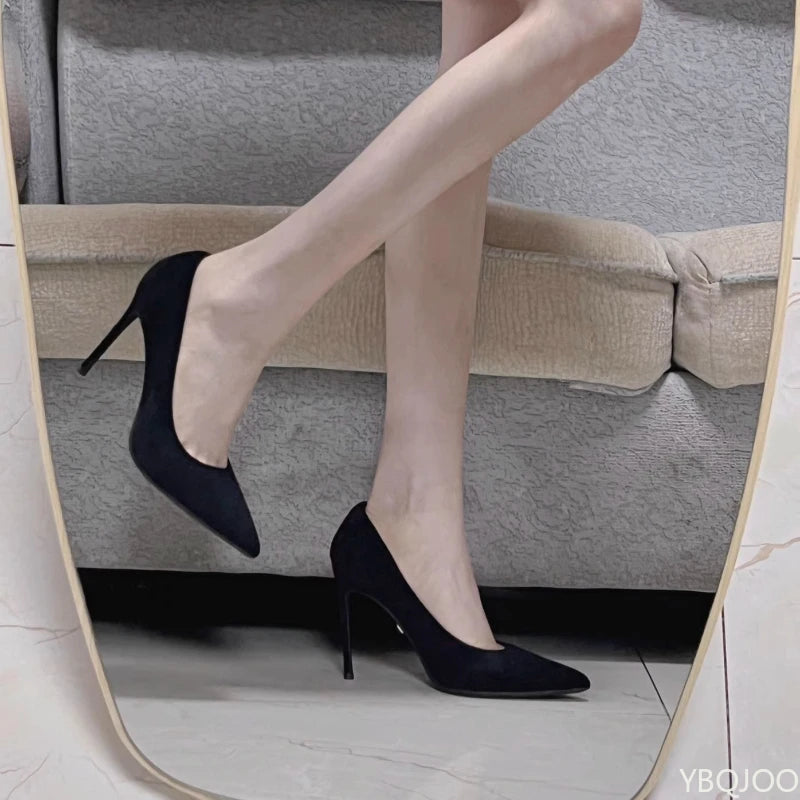 Black high-heeled shoes worn with beige pants in a mirror reflection.