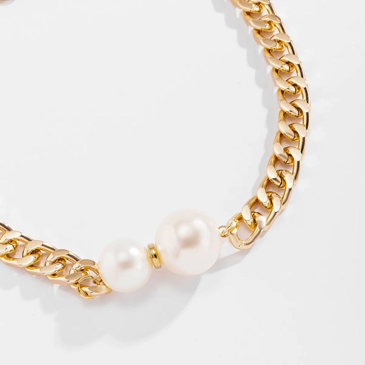 Gold chain necklace with pearls worn by a person in a white shirt.