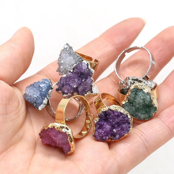 Hand holding multiple gemstone rings with gold and silver bands on a white background