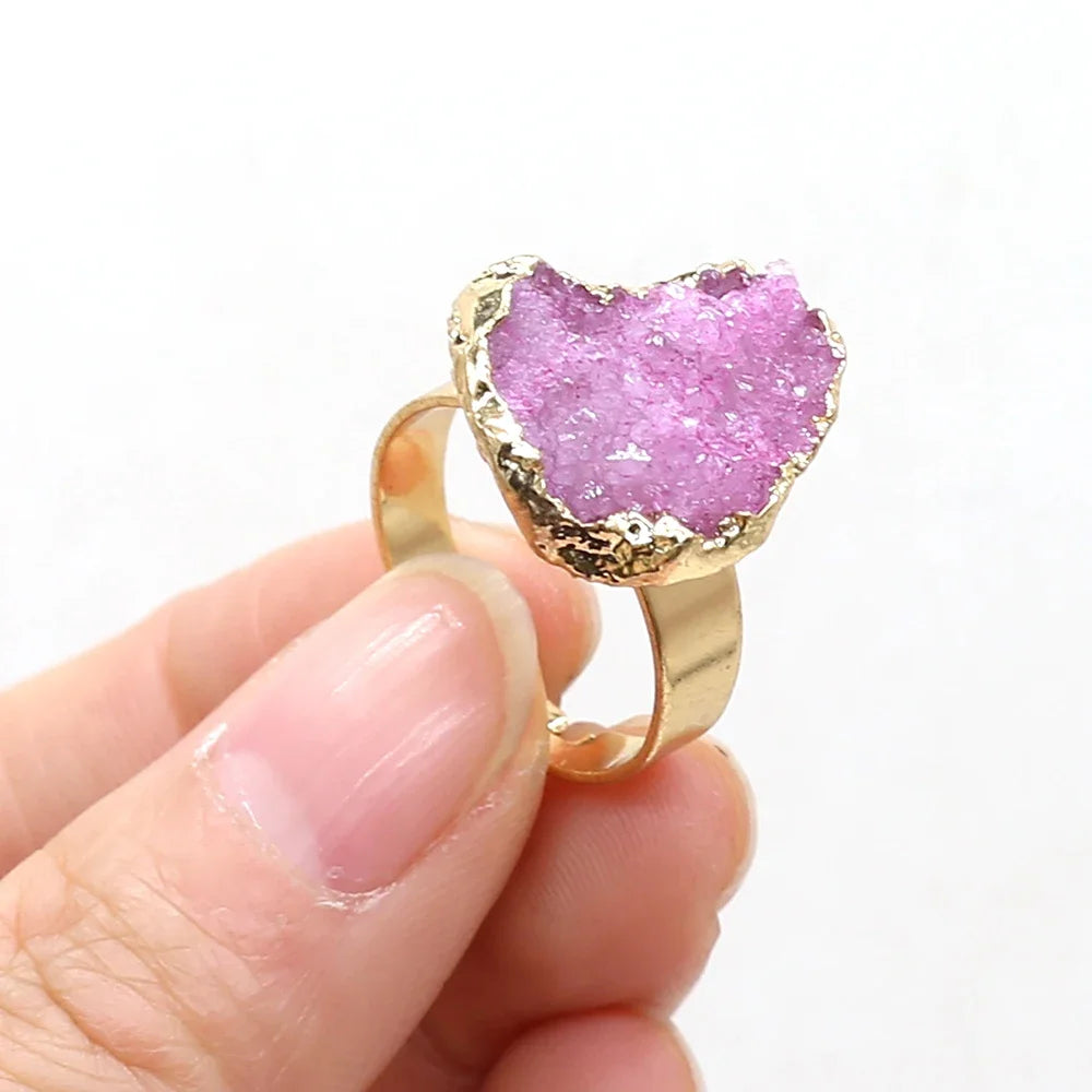Pink druzy ring with gold band held by a hand on a white background