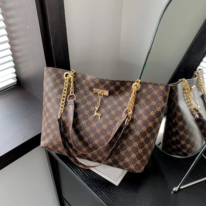 Women’s leather tote bag in brown monogram plaid with gold chain handles and hanging charms.