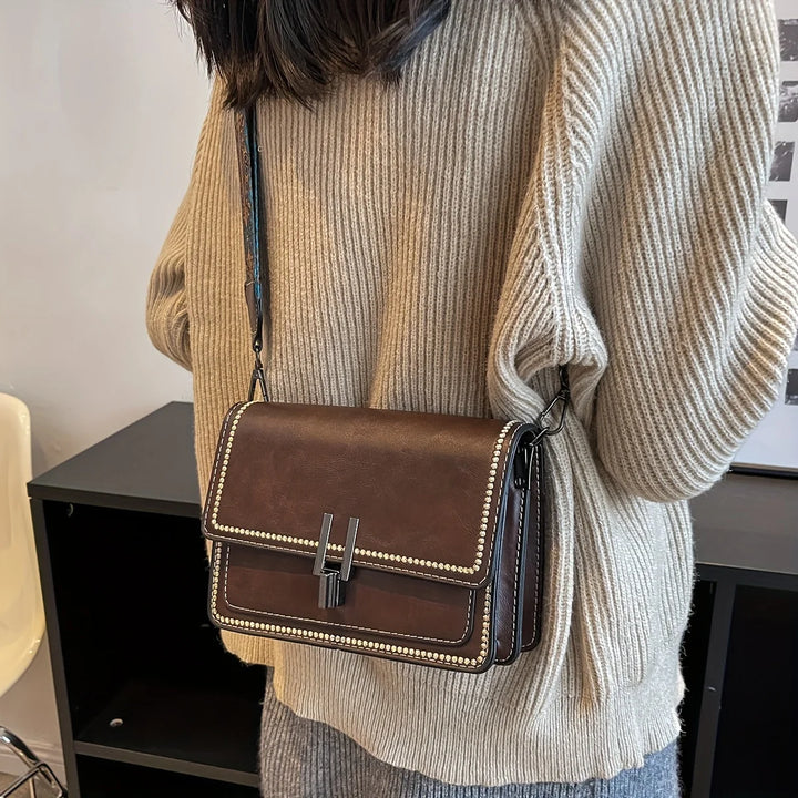Mini crossbody bag in brown with flap lock, beaded trim, and long adjustable shoulder strap