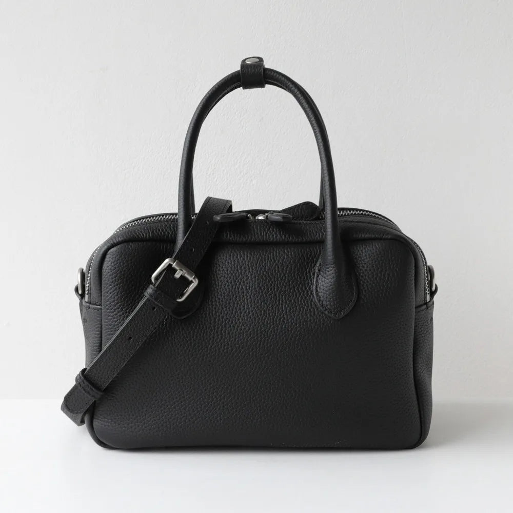 A black pebbled leather handbag with dual top handles and a detachable shoulder strap, photographed against a plain light gray background.