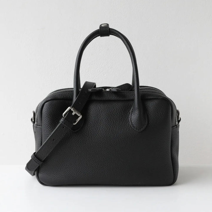 A black pebbled leather handbag with dual top handles and a detachable shoulder strap, photographed against a plain light gray background.