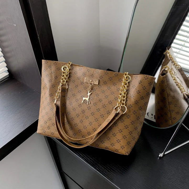 Women’s leather tote bag in tan monogram plaid with gold chain handles and hanging charms.