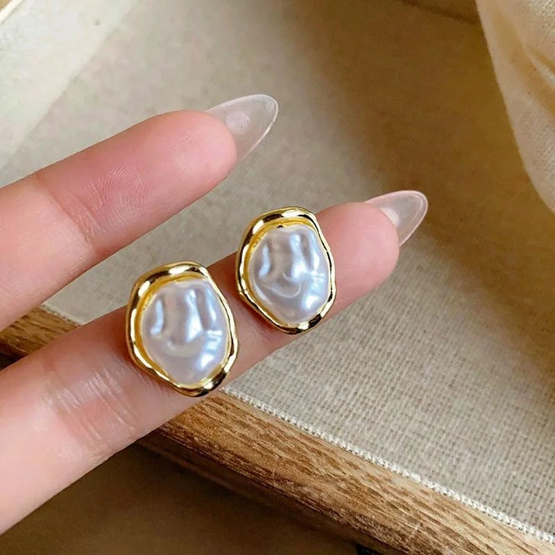 Pearl earrings with gold frames held between fingers on a neutral background
