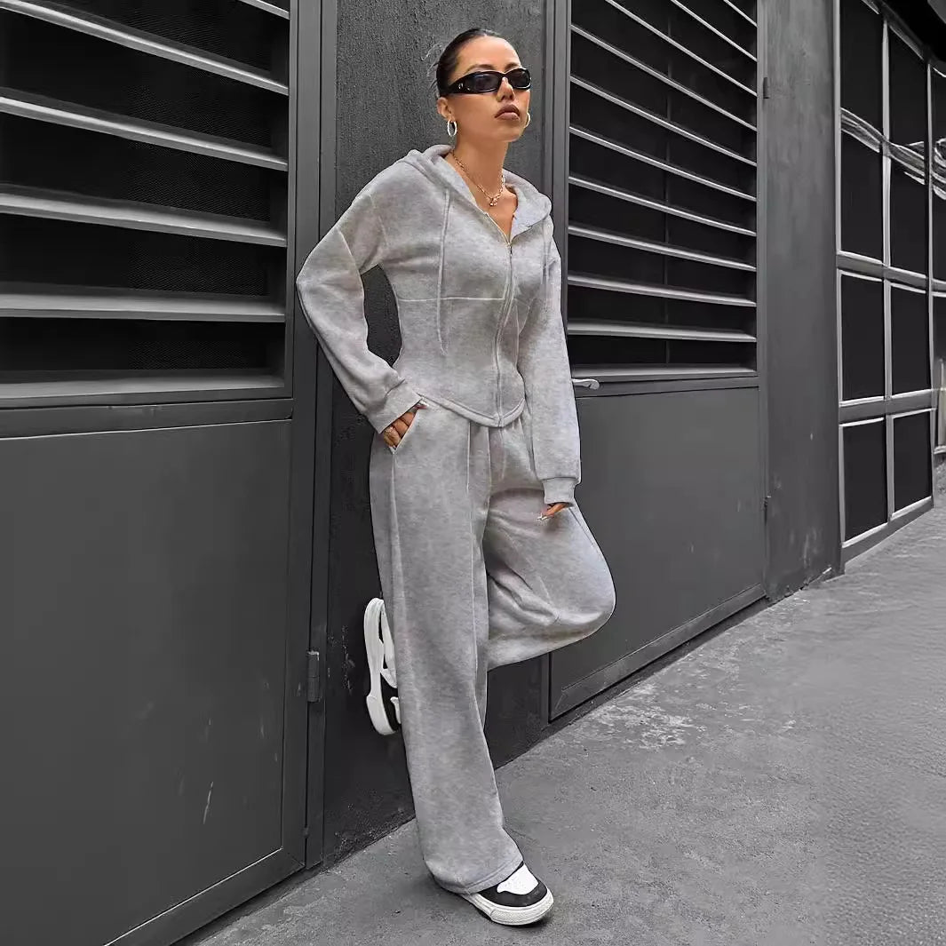 Person wearing a gray tracksuit standing against a dark wall.