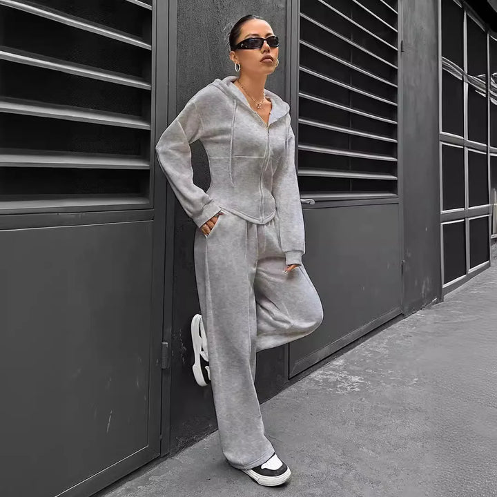 Person wearing a gray tracksuit standing against a dark wall.