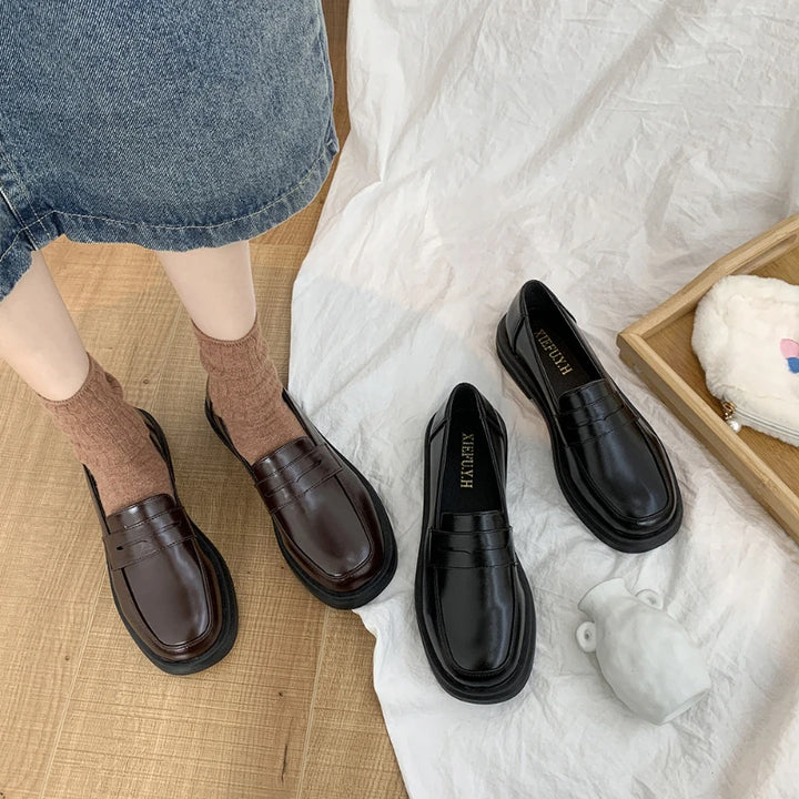 Brown and black loafers on a wooden floor with a white textured rug.