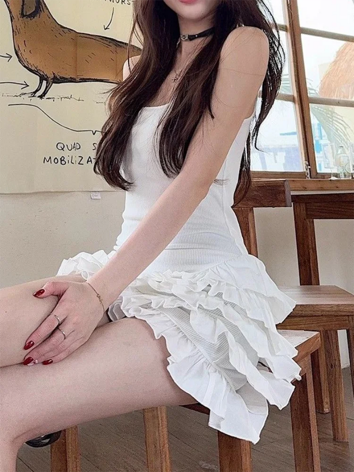 Woman in a white dress sitting on a wooden chair indoors.