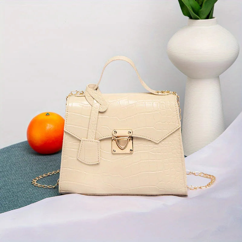 Beige handbag with gold accents on a surface with an orange and vase in the background