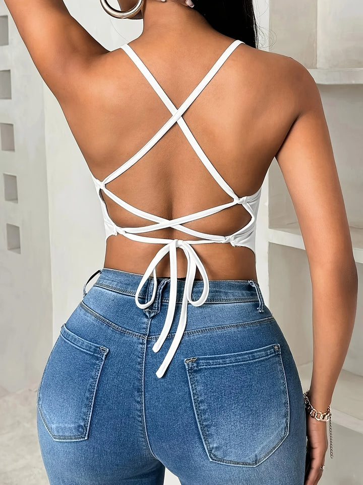 Person wearing a white strappy top and blue jeans with a neutral background
