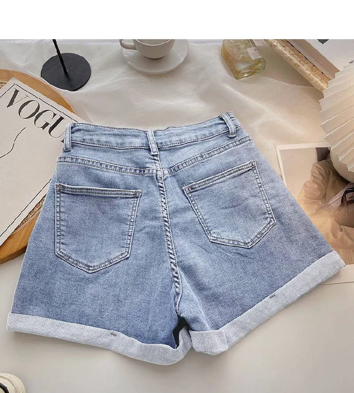 Light blue denim shorts on a white surface with a magazine and cup in the background