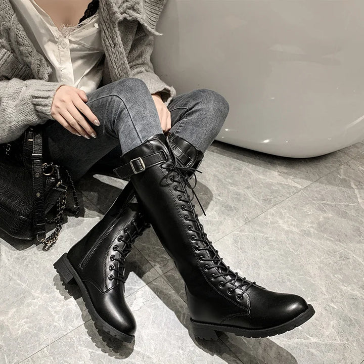 Person wearing black knee-high boots sitting on a bench.
