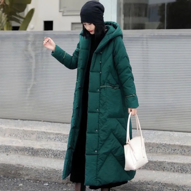 Person wearing a long green coat standing on steps with a neutral background