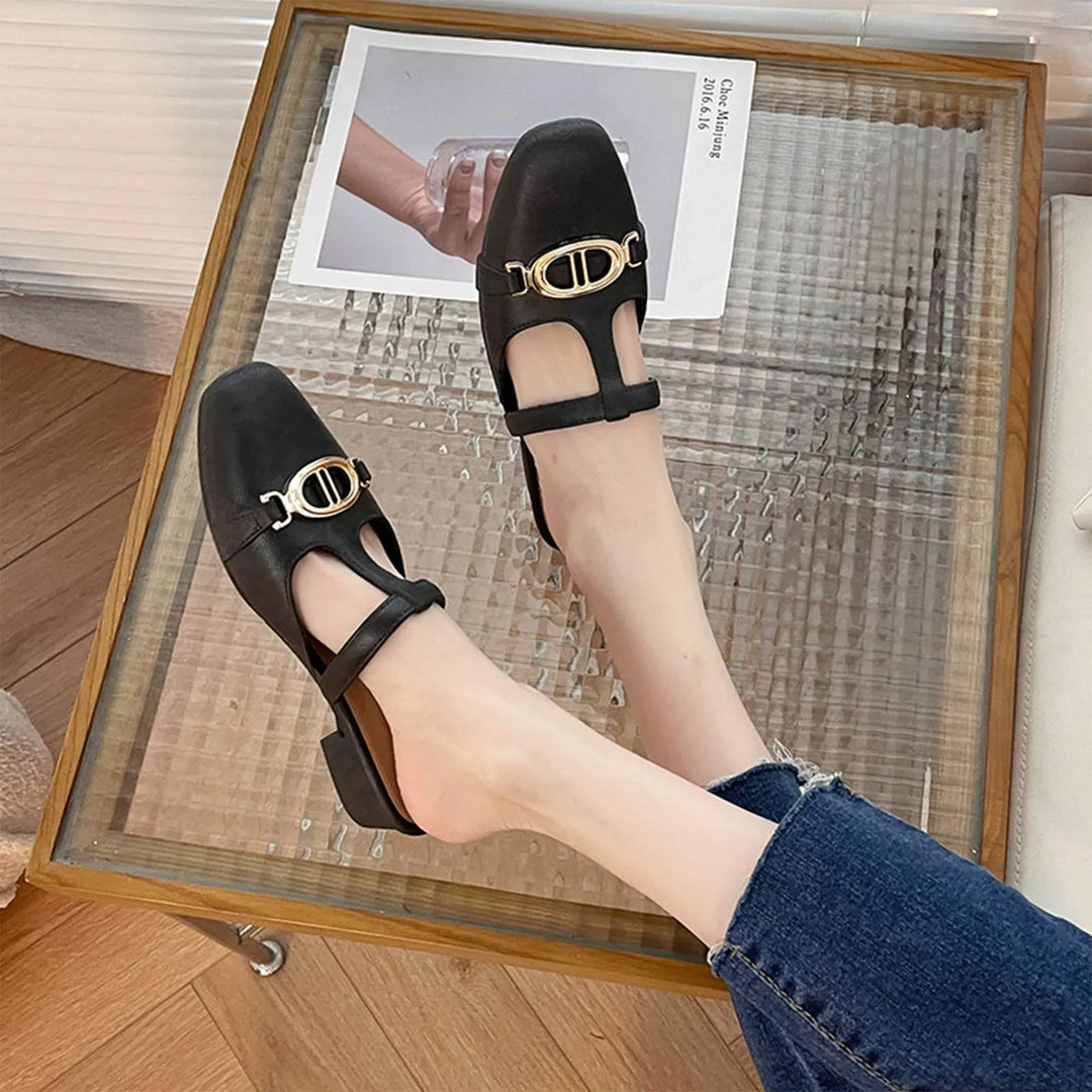 Black shoes with gold buckles worn by a person on a wooden floor.