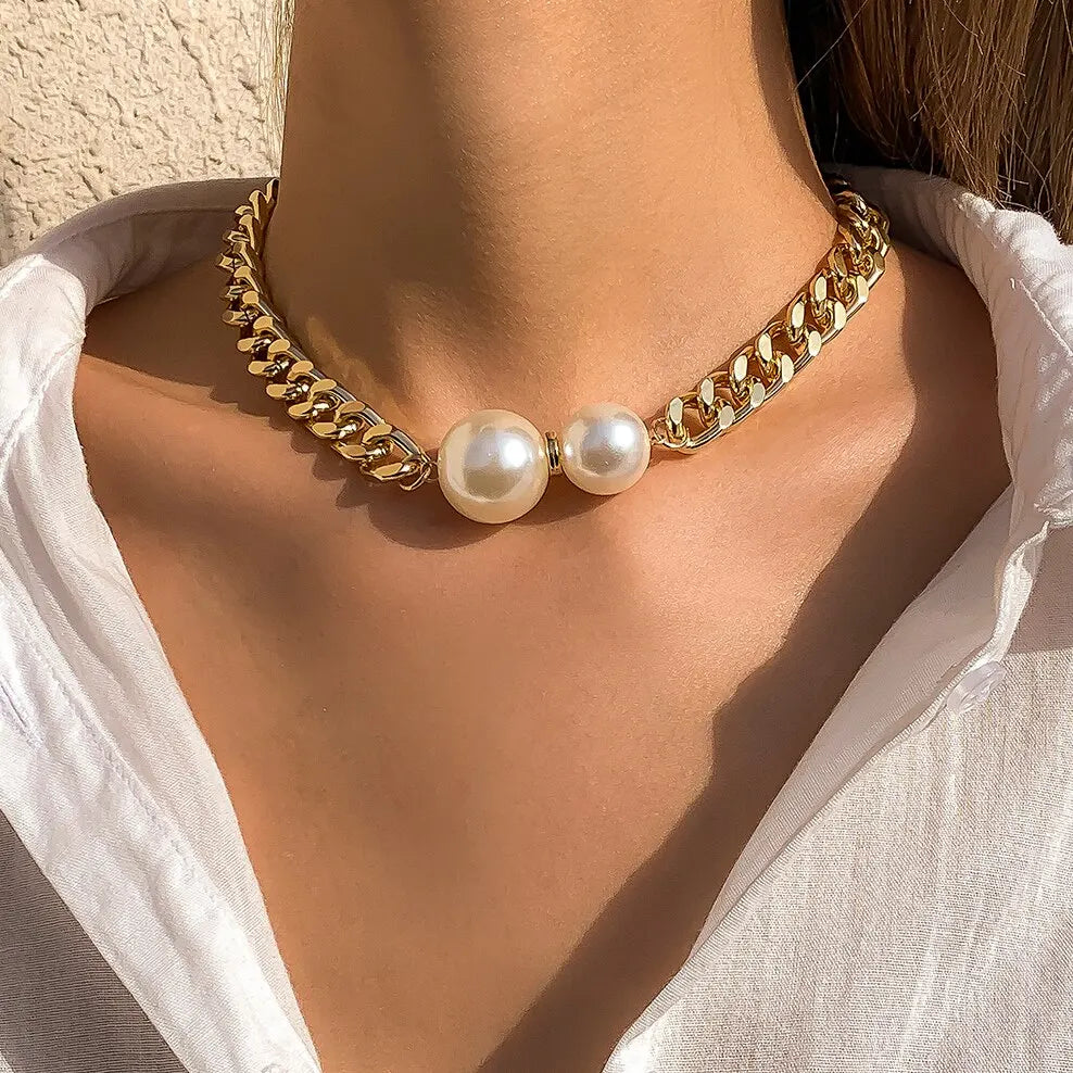 Gold chain necklace with pearls worn by a person in a white shirt.
