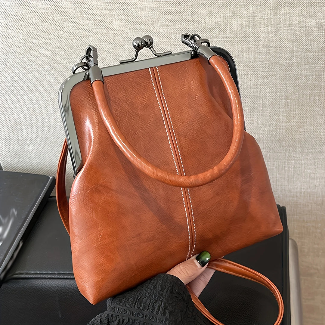 Brown leather handbag with a metal frame held by a hand against a neutral background