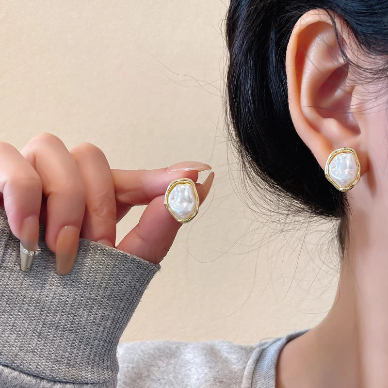 Close-up of a person wearing gold earrings with pearl-like stones on a beige background