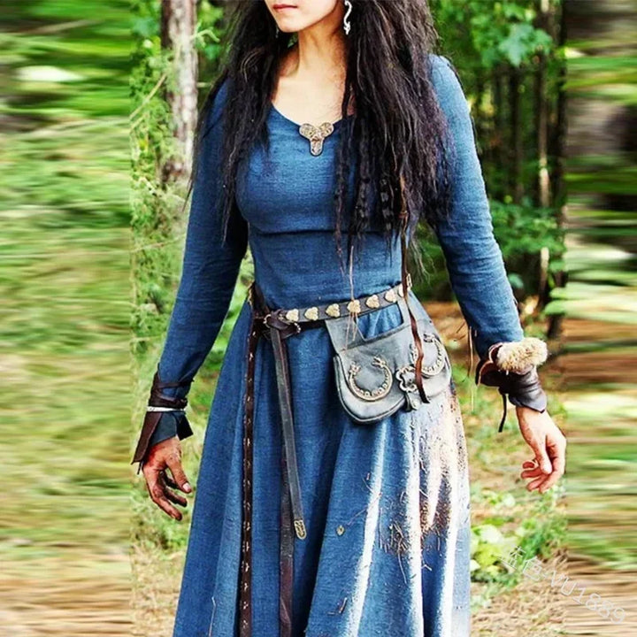 Person in a blue medieval-style dress with accessories standing in a forest.