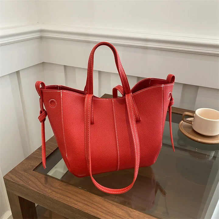 Red handbag on a wooden surface with a white wall background