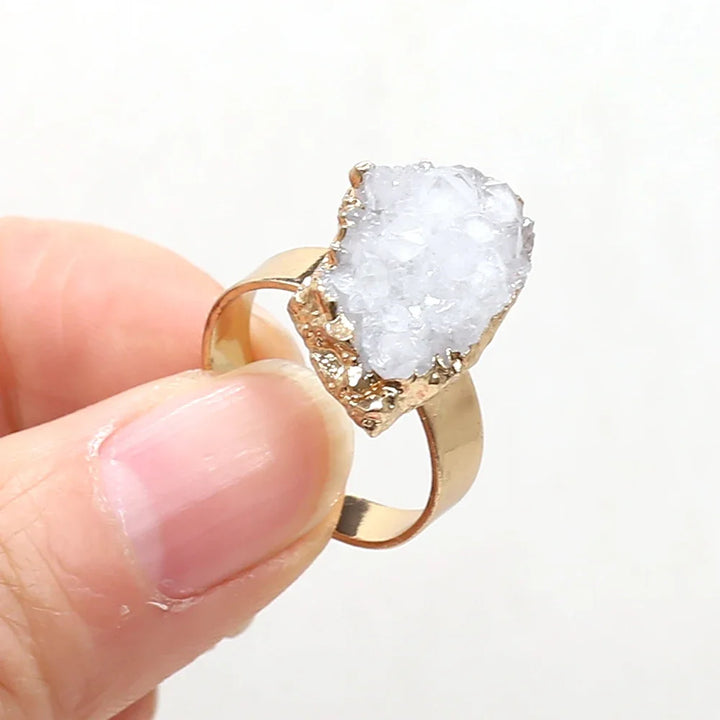 Gold ring with a large, clear crystal held by a hand against a white background