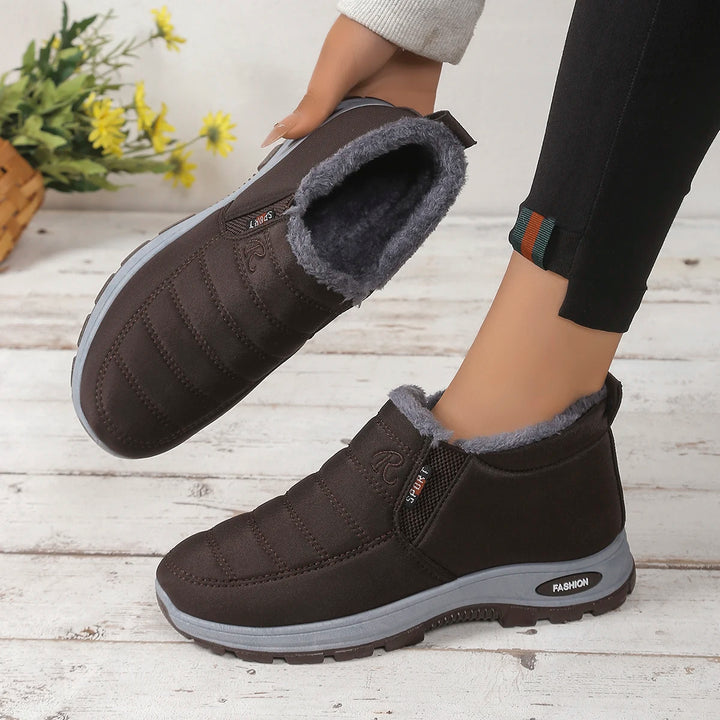 Person wearing black slip-on boots with gray lining on a wooden floor.