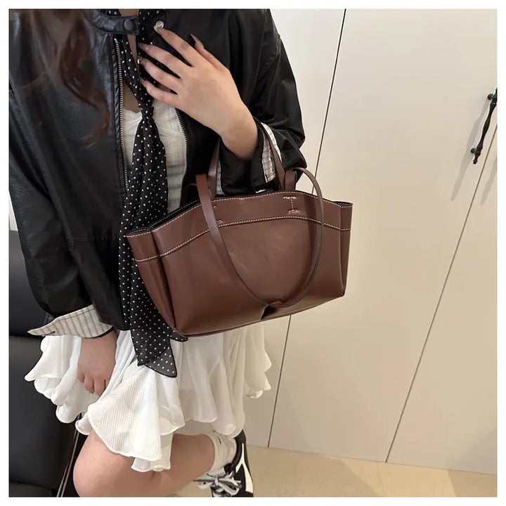 Person holding a brown handbag with a neutral background