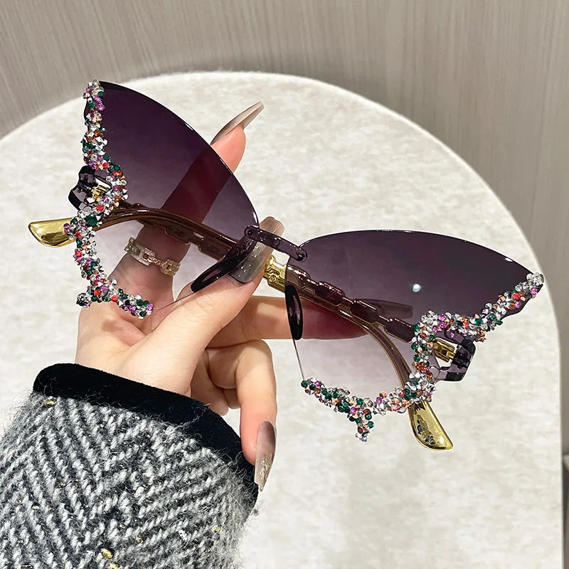 Sunglasses with decorative embellishments held by a hand against a neutral background