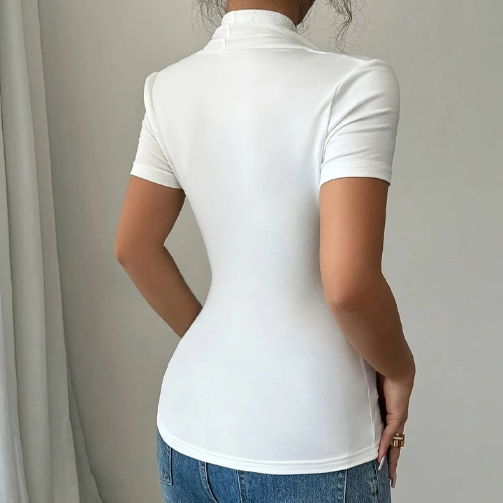 Person wearing a white turtleneck and blue jeans against a neutral background