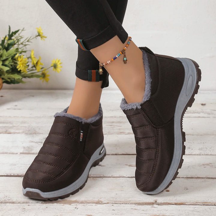 Black winter boots with gray soles worn by a person on a wooden floor.