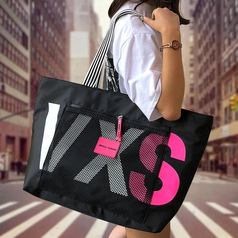 Black waterproof nylon tote bag with large pink letter print and mesh laptop compartment