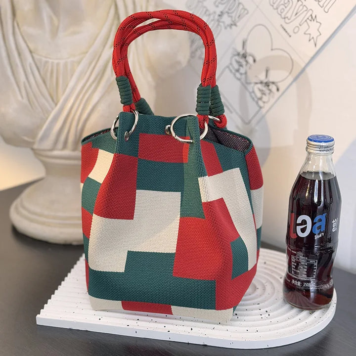 Color-block satchel bag with red top handles and teal/white/red square panels.