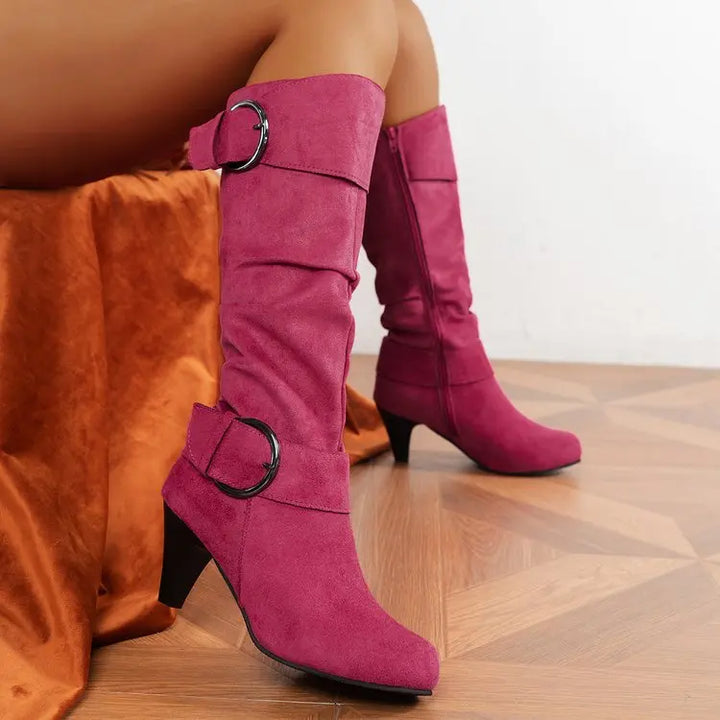 Pink knee-high boots with buckles worn by a person on a wooden floor.