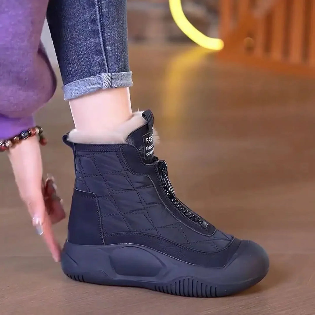 Black winter boot worn by a person on a wooden floor.