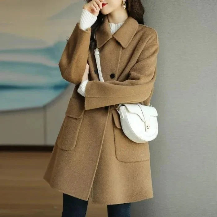 Person wearing a brown coat with a white handbag against a neutral background