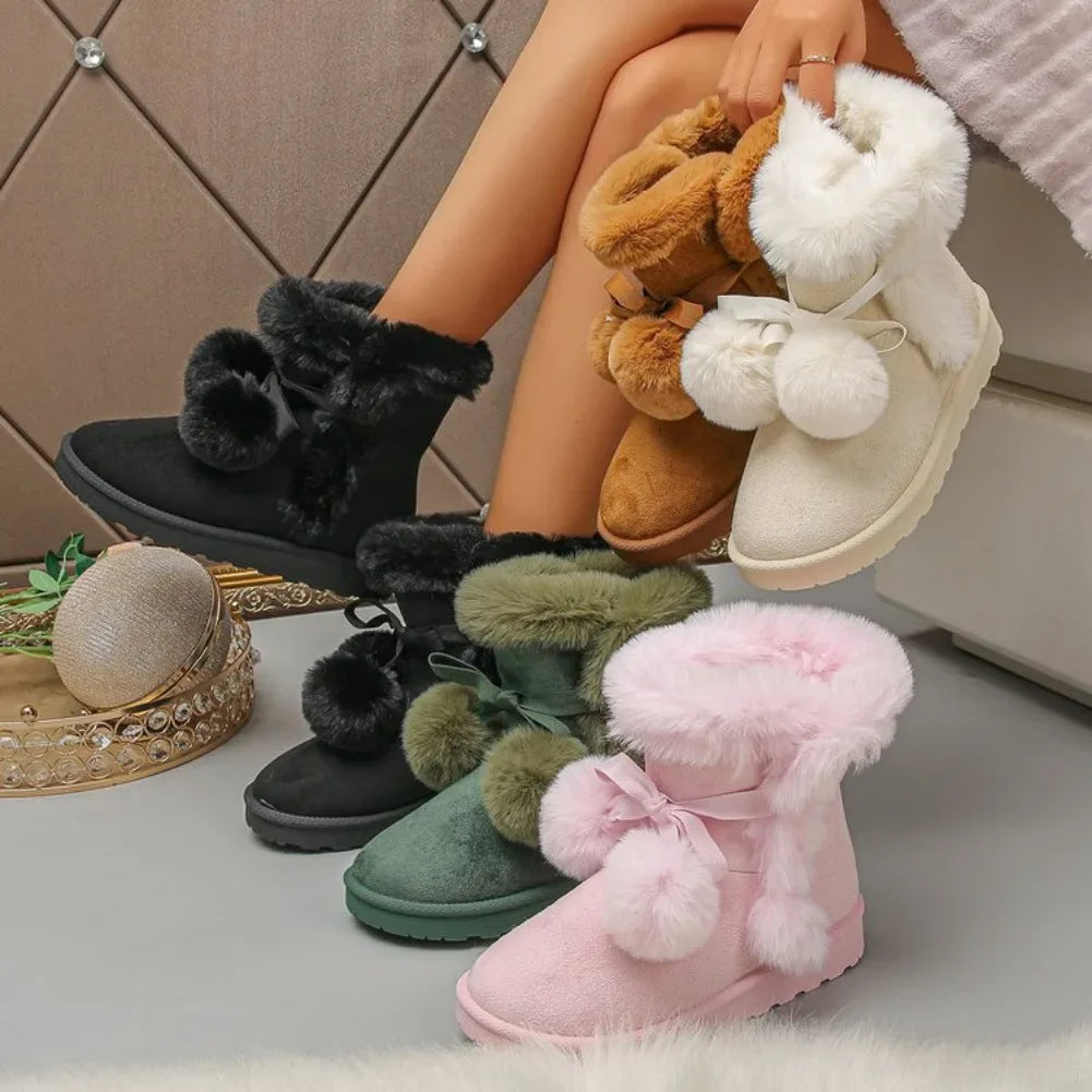 Four women's plush faux-fur ankle boots are shown in a lifestyle setting, with a model's legs crossed holding two brown and cream versions, while two more are placed on the floor in green and pink. The boots feature fluffy pom-poms, bows, and thick soles.