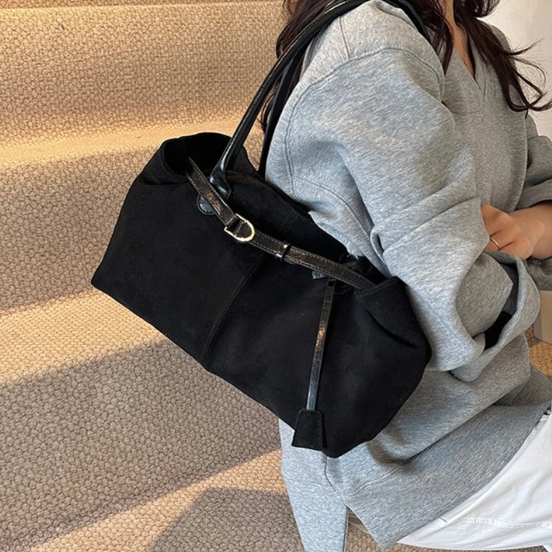 Women’s suede tote bag in black with short handles and adjustable tassel strap.