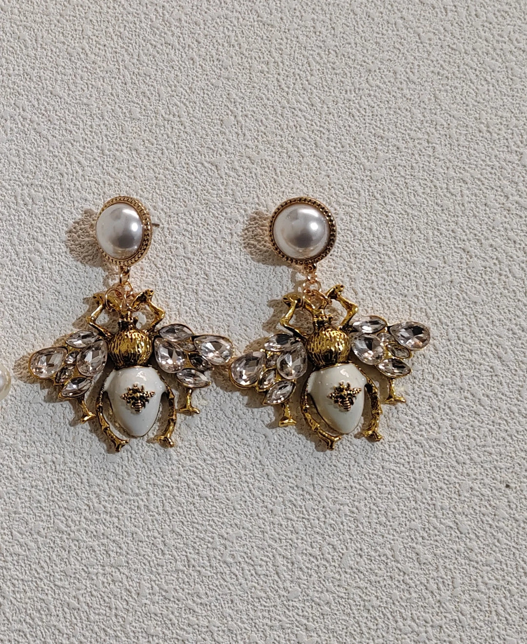 Pair of ornate earrings with gold and pearl details on a light gray background