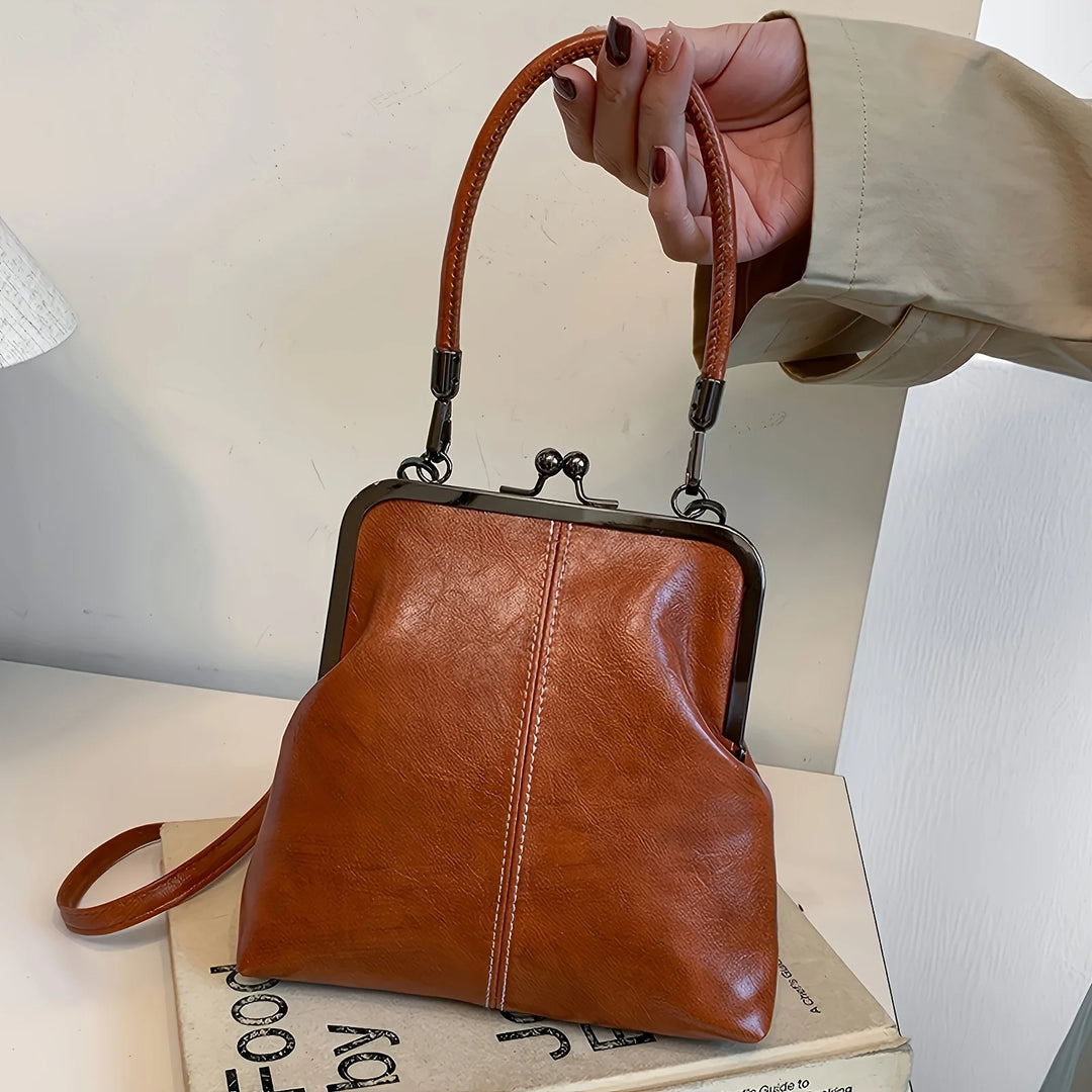 Brown leather handbag held by a hand on a light background
