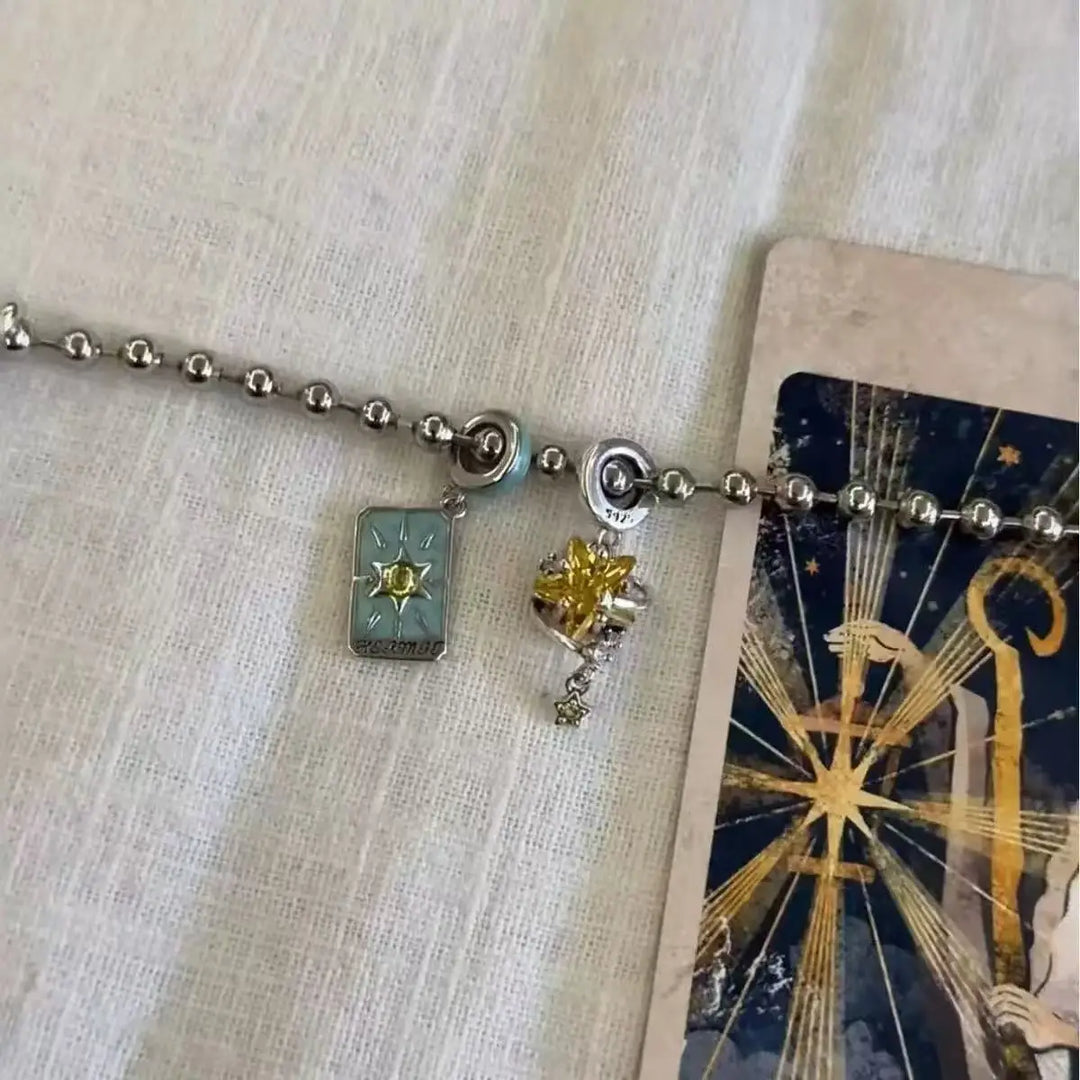 Necklace with charms on a textured surface next to a tarot card