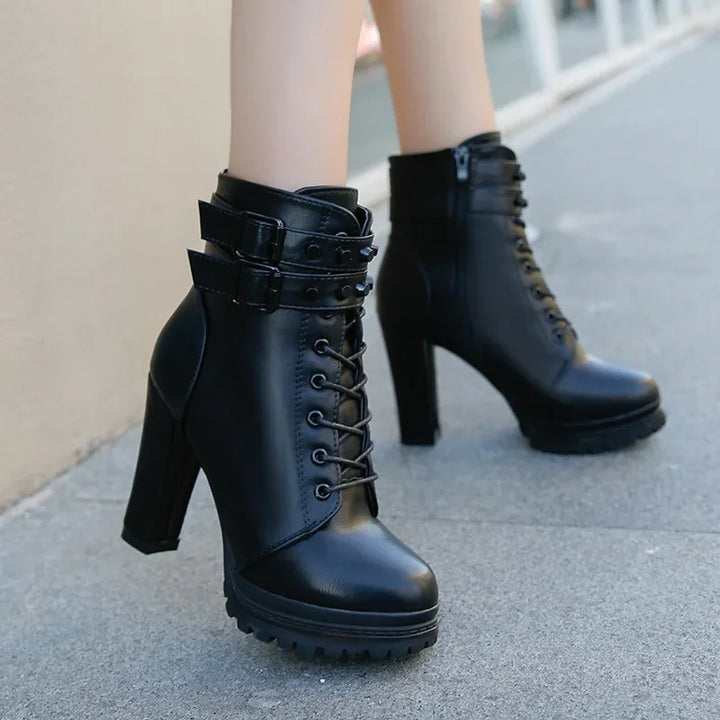 Black high-heeled boots with buckle details on a pavement background