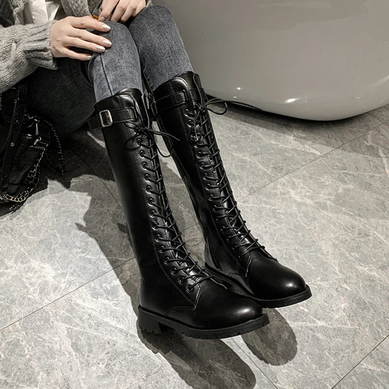 Person wearing black knee-high boots with laces on a tiled floor.