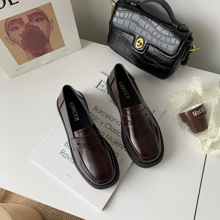 Brown loafers on a magazine with a black handbag and coffee cup in the background